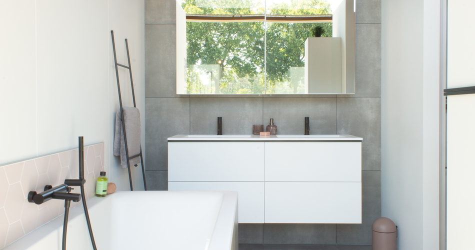 Salle de bain de style moderne avec meuble de salle de bain blanc, robinetterie noire, carrelage gris et baignoire îlot avec douchette noire.