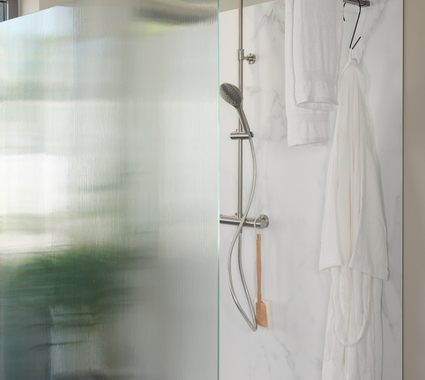 Douche à l’italienne avec paroi en verre nervuré et panneau mural effet marbre, équipée d’une douche moderne et d’un porte-serviettes.