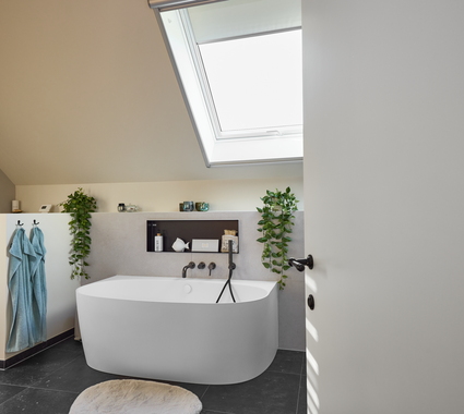 Rénovation de salle de bain moderne avec baignoire adossée au mur sous une fenêtre de toit, accents noirs et plantes vertes pour une ambiance fraîche.