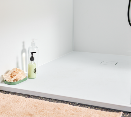Douche à l’italienne avec panneau mural en acrylique blanc et receveur de douche, équipée de produits de soin et d’une douchette noire pour une finition épurée.