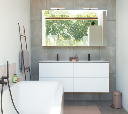 Salle de bain de style moderne avec meuble de salle de bain blanc, robinetterie noire, carrelage gris et baignoire îlot avec douchette noire.