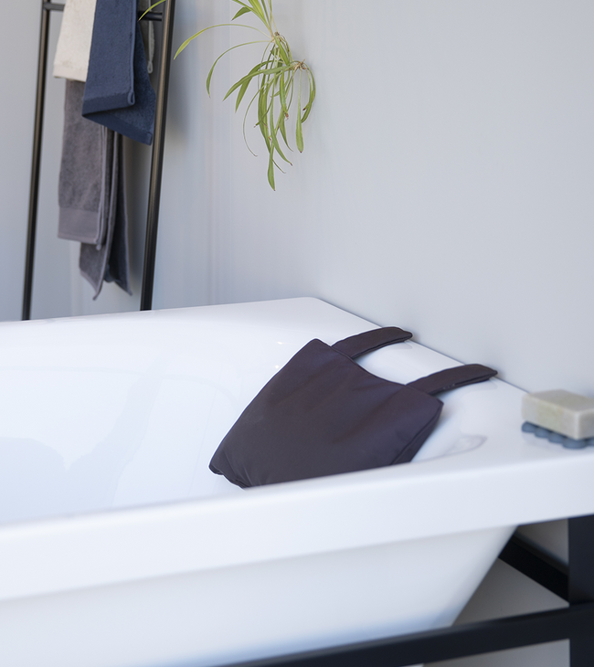 Baignoire îlot de style moderne avec structure en métal noir, coussin de bain noir et finition minimaliste, contre un mur gris clair