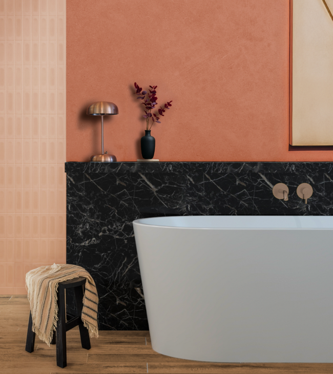 Baignoire îlot avec mur arrière en marbre noir, robinet couleur cuivre et mur terracotta chaleureux dans une salle de bain élégante.