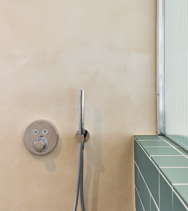 Mur de doublage mi-hauteur avec carreaux verts et robinetterie de douche encastrée dans une salle de bain épurée et minimaliste.
