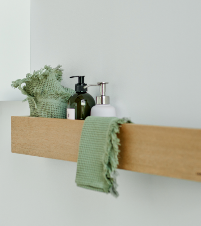 Étagère en bois dans la salle de bain avec des distributeurs de savon, un gant de toilette vert et une serviette, pour une ambiance naturelle et ordonnée.