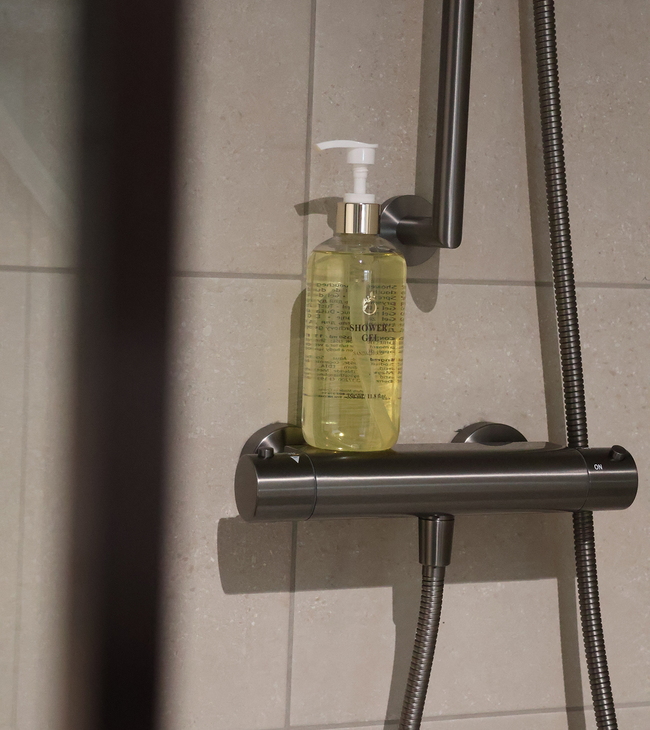 Mitigeur de douche avec finition gunmetal et gel douche, installé contre un mur carrelé pour un entretien facile dans la salle de bain.