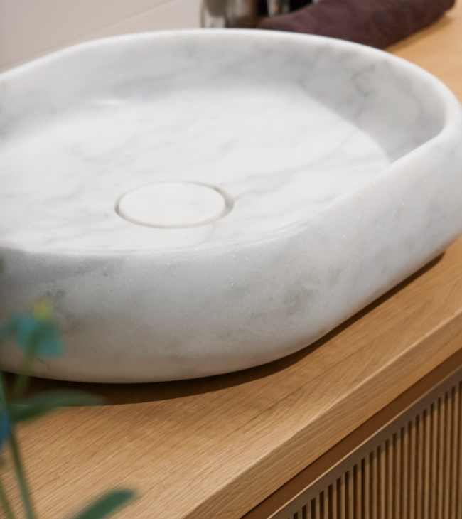 Vasque à poser en marbre de Carrare sur meuble en bois, avec un aspect naturel adapté à une salle de bain au design biophilique.