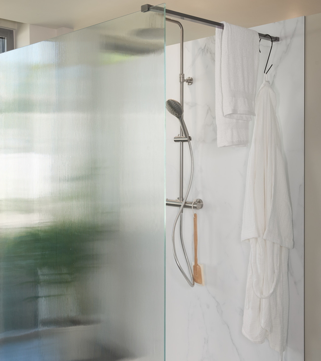 Douche à l’italienne avec paroi en verre nervuré et panneau mural effet marbre, équipée d’une douche moderne et d’un porte-serviettes.