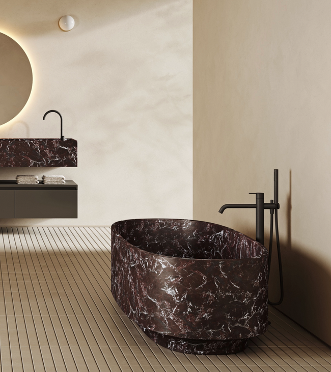 Salle de bain luxueuse avec baignoire îlot en marbre rouge et vasque assortie, contre un mur et un sol beiges.