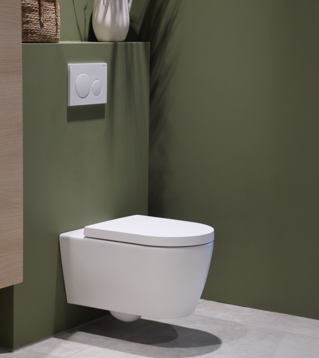 WC suspendu blanc avec plaque de commande Geberit, installé contre un mur vert élégant dans une salle de bain au design biophilique.