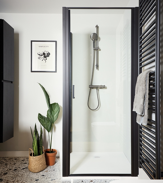 Salle de bain moderne avec porte de douche à cadre noir, sol en terrazzo et radiateur porte-serviettes noir à côté de la douche.