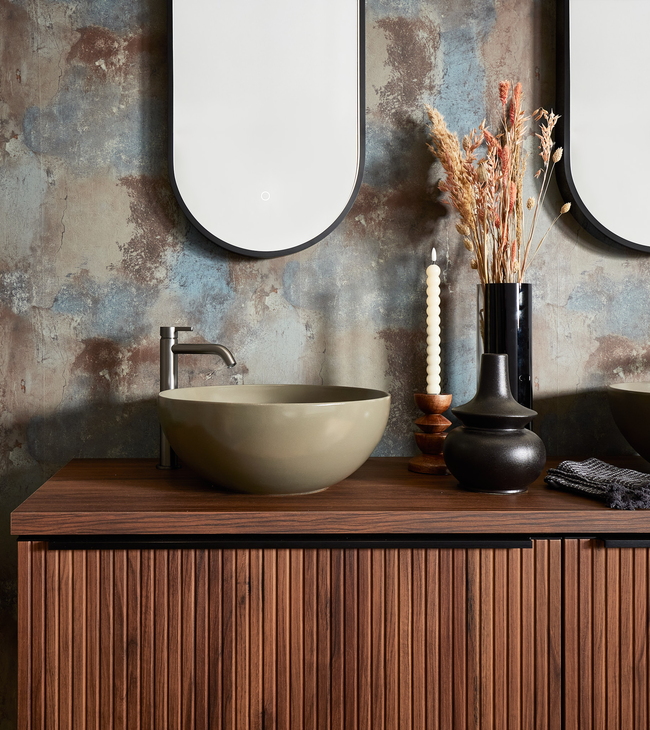 Meuble de salle de bain de style urban industrial avec bois de noyer nervuré, vasque à poser, miroir ovale et accessoires décoratifs.