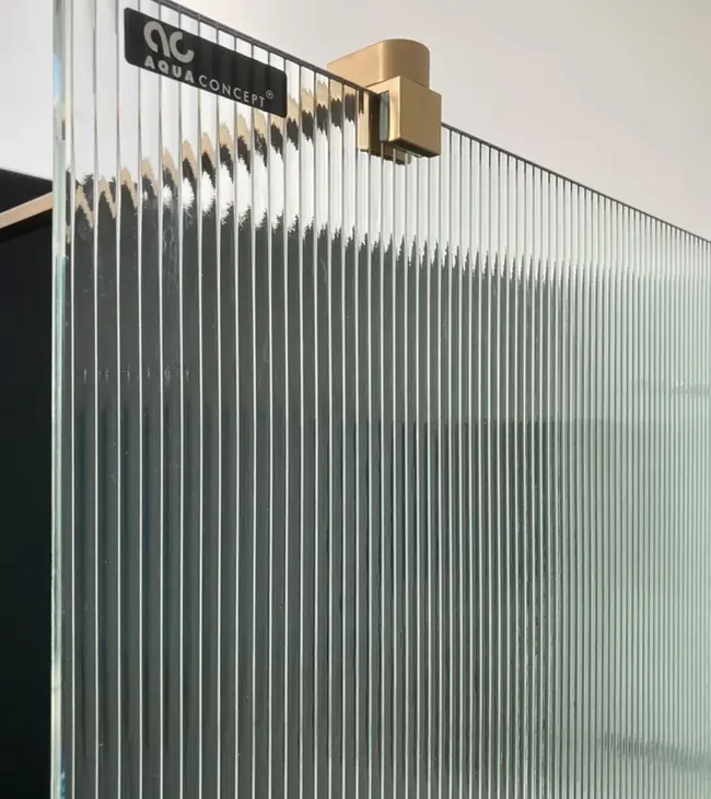 Détail d’une paroi de douche en verre nervuré avec une fixation murale dorée de Aquaconcept.