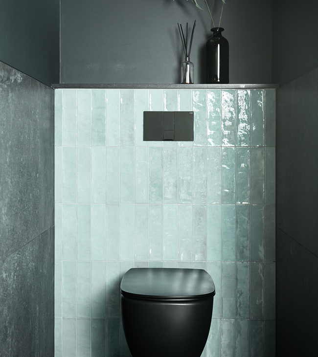 Toilet moderne avec cuvette noire, carrelage vert sur le mur arrière et murs foncés pour un contraste élégant.