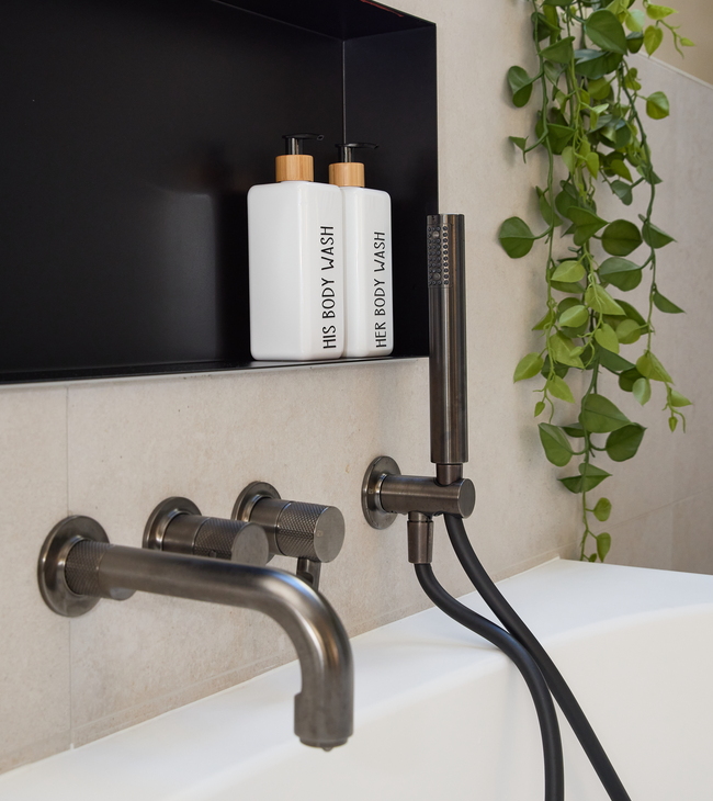 Détail d’une baignoire moderne avec robinetterie noire et mur à niche, dans une salle de bain élégante et rénovée avec des accents verts.