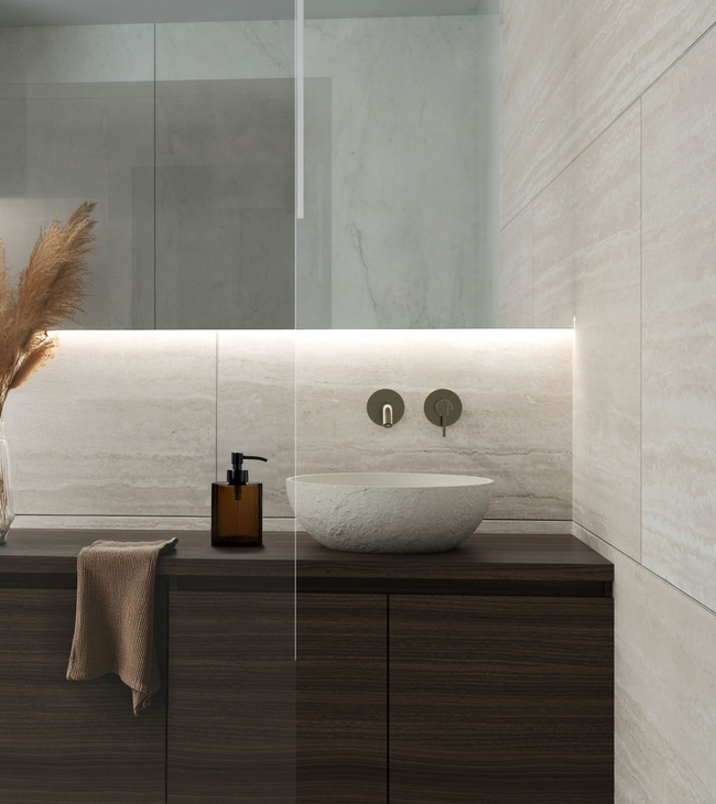 Meuble de salle de bain avec vasque, robinet encastré et mur revêtu de carreaux en travertin avec éclairage LED subtil.