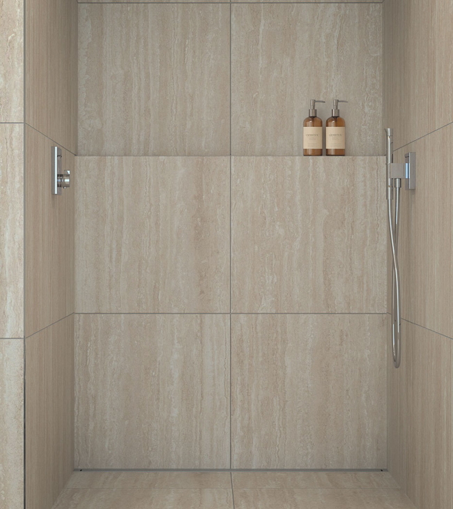 Douche à l’italienne avec grands carreaux en travertin, niche pour shampooing et robinetterie encastrée épurée en chrome.