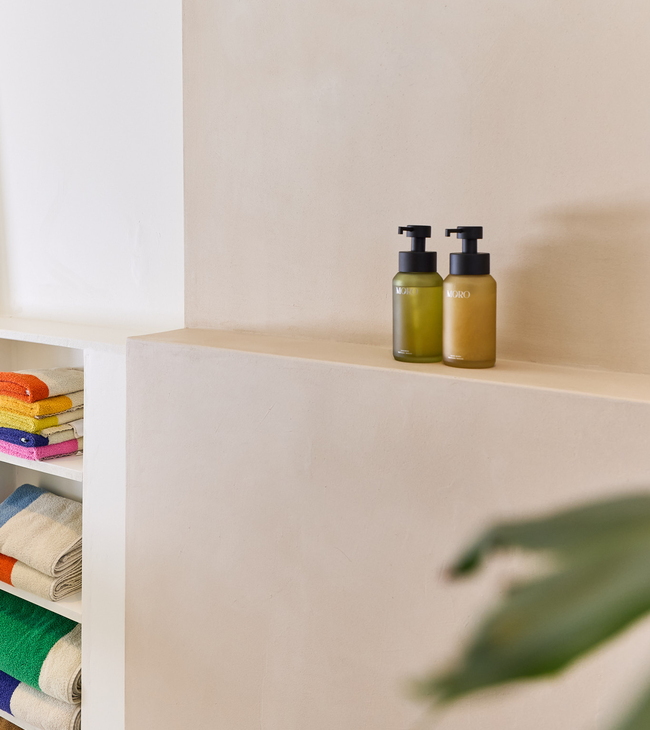 Mur en mortex dans la salle de bain avec serviettes colorées et deux distributeurs de savon élégants sur une étagère de niche.