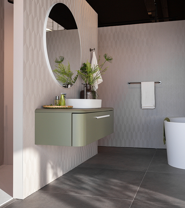 Salle de bain de style moderne avec meuble suspendu vert, miroir rond, douche à l’italienne et baignoire îlot au design élégant.