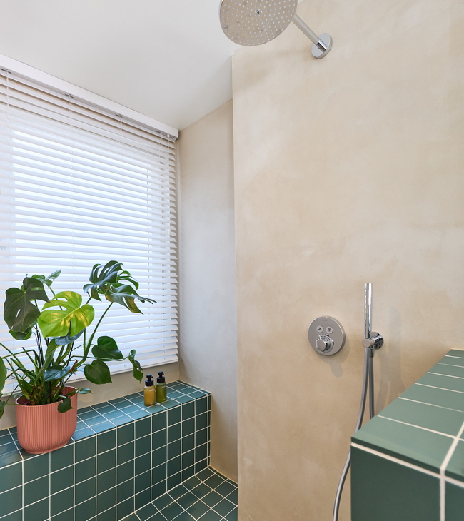 Douche à effet pluie avec robinet encastré, murs en mortex et carreaux verts dans une douche moderne avec plantes et lumière naturelle.