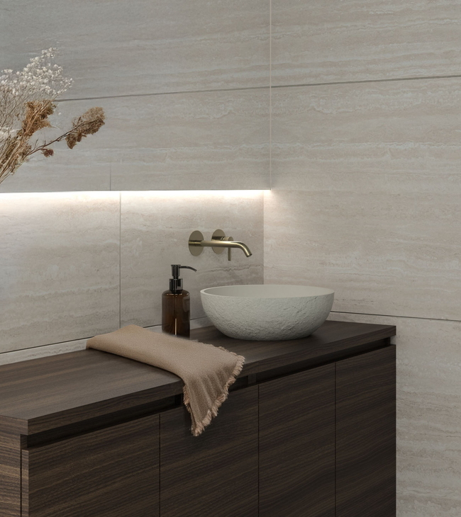 Salle de bain de style minimaliste avec meuble en bois foncé, vasque ronde, carreaux muraux en travertin et éclairage indirect.