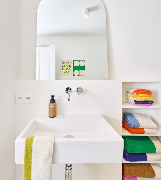 Vasque suspendue avec robinet encastré, serviettes colorées dans une niche et grand miroir dans une salle de bain moderne.