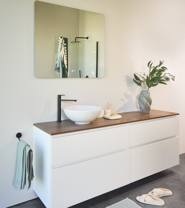 Intérieur de salle de bain nordique avec meuble laqué blanc, plan en bois, vasque à poser, robinet noir et miroir rond.