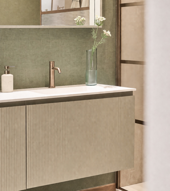 Salle de bains avec un meuble de salle de bains vert sauge, équipé d'une robinetterie en bronze et d'une douche en verre nervuré, ainsi que de profilés couleur bronze, le tout sur un mur vert sauge
