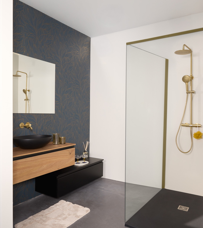Salle de bains chic d'hôtel, avec un meuble-lavabo asymétrique composé d'un meuble en bois et d'un meuble noir suspendu légèrement plus bas. Sur le meuble en bois repose un lavabo noir à poser, accompagné d'une robinetterie dorée assortie. L'ensemble est complété par un grand miroir rectangulaire.