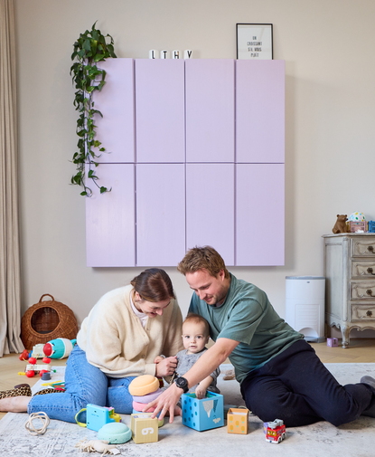 Témoignage d’un jeune couple jouant avec leur bébé par terre, entouré de jouets colorés dans un salon chaleureux.