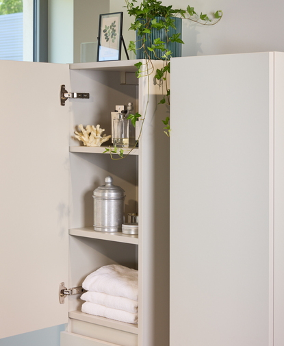 Armoire colonne beige pour la salle de bain, avec portes ouvertes dans un modèle peu profond afin de gagner de la place dans les petites salles de bain.