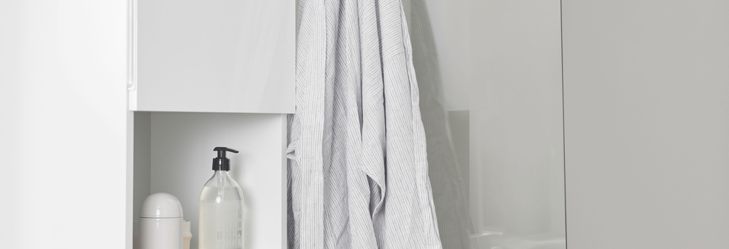 Baignoire blanche avec paroi de douche en verre et robinet chromé, à côté d’une armoire blanche et d’accessoires pour un look frais et moderne de salle de bain.