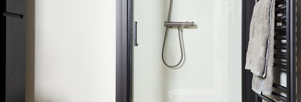 Cabine de douche épurée avec profils noirs et porte en verre, équipée d’une douche à effet pluie moderne et d’un sol en bois.