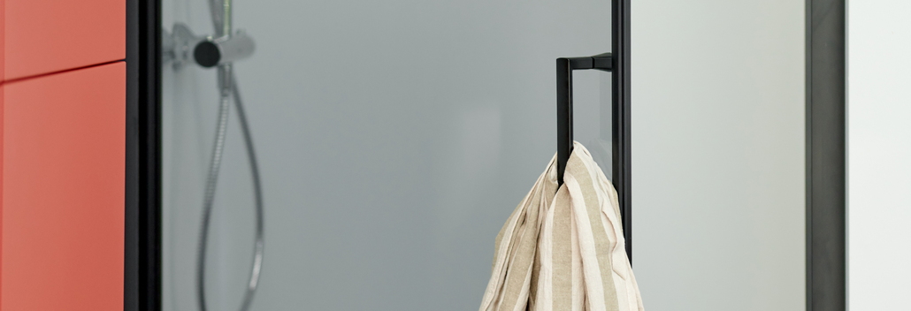 Porte de douche moderne avec poignée noire, à côté d’une armoire rouge et d’une plante verte, donnant à la salle de bain un look épuré et élégant.