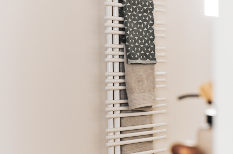Radiateur design blanc avec serviettes servant de chauffage de salle de bain, détail moderne et fonctionnel dans une salle de bain lumineuse.